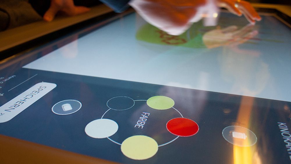 An interactive surface showing a digital color palette and a drawing canvas. Fingers drawing on the canvas.