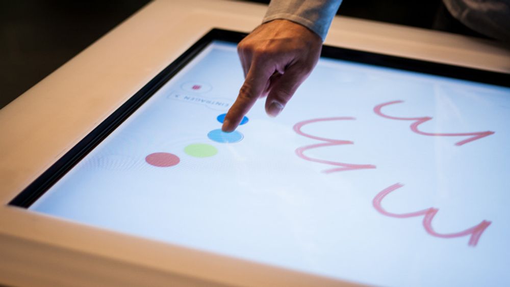 An interactive surface showing a digital color palette and a drawing canvas. Fingers drawing on the canvas.